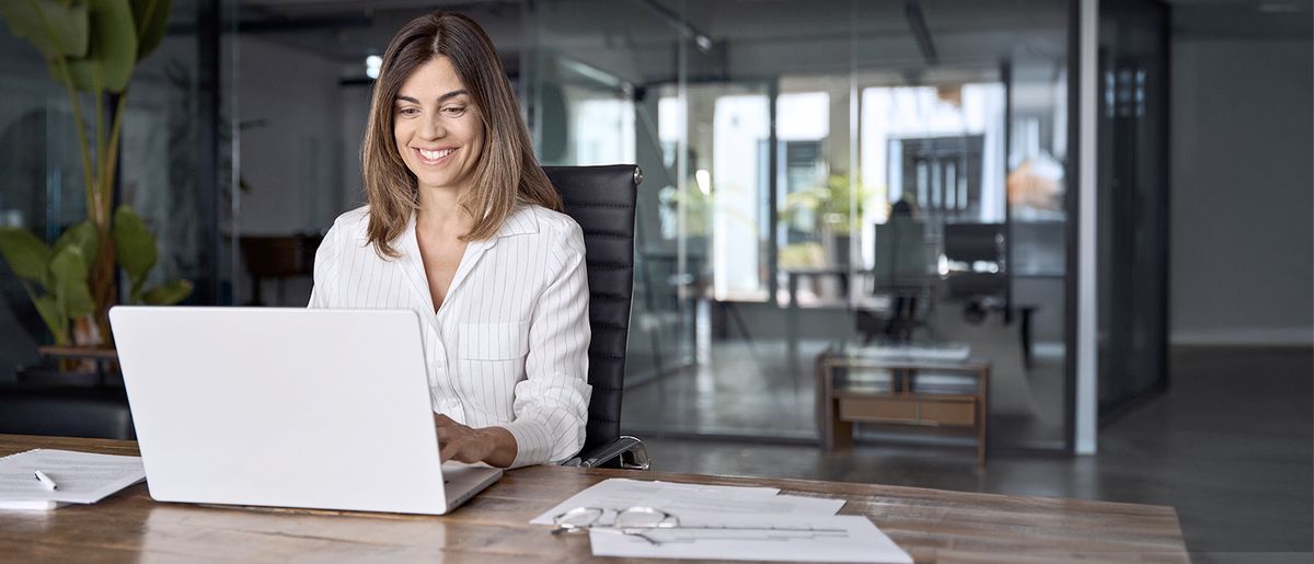 eine Frau arbeitet an ihrem Laptop an einem Schreibtisch in einem Bürogebäude