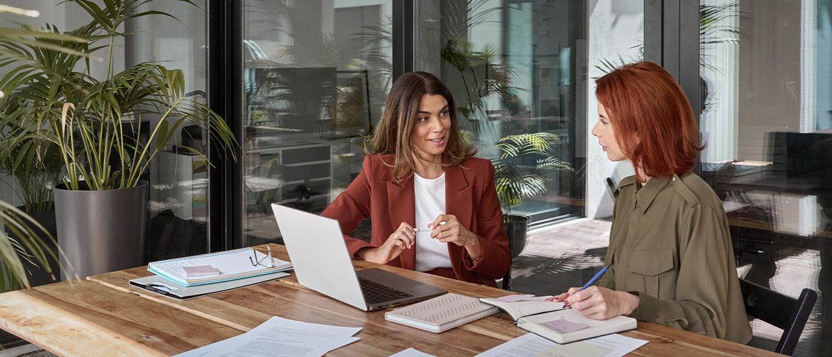 Two employees are discussing while sitting on a desk