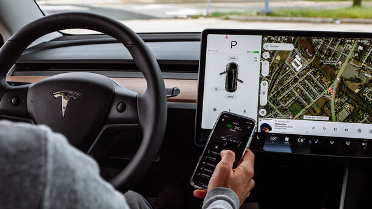 Innenansicht eines Tesla Model Y in der eine Person ein Smartphone mit der Tesla App in der Hand hat