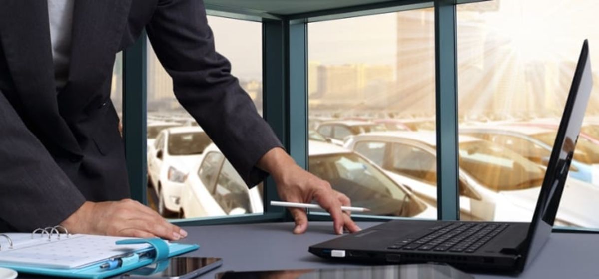 Una persona de negocios señalando una laptop en un escritorio con vistas a un aparcamiento lleno de coches
