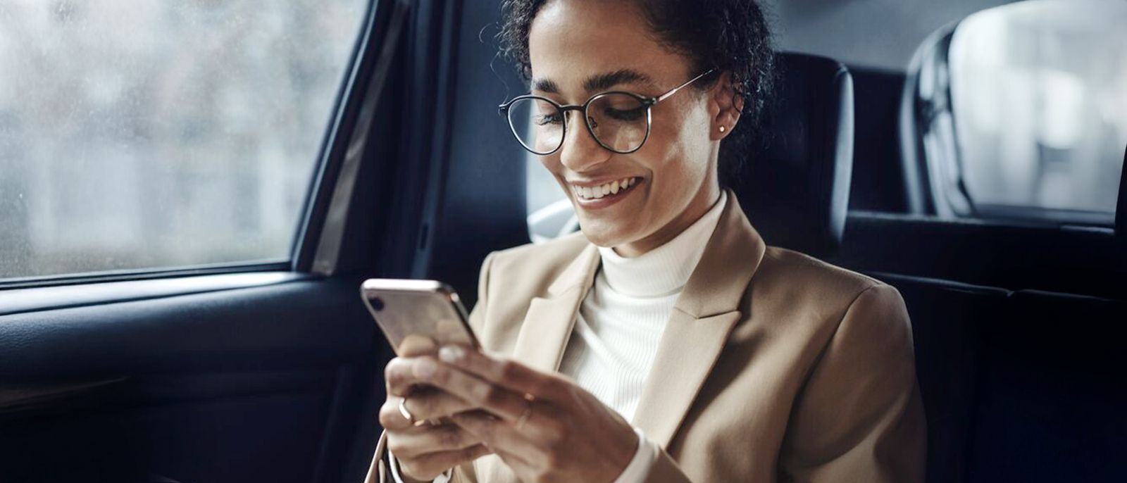 Woman sitting on the back seat of a car and typing into her smartphone