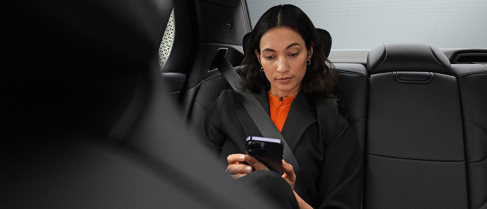 Eine Geschäftsfrau sitzt hinten im Auto und schaut in Ihr Smartphone faltet Stoffe