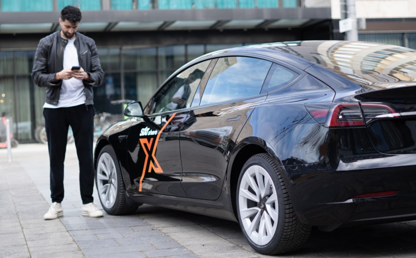 Ein Mann steht vor einem SIXT Fahrzeug mit einem Smartphone