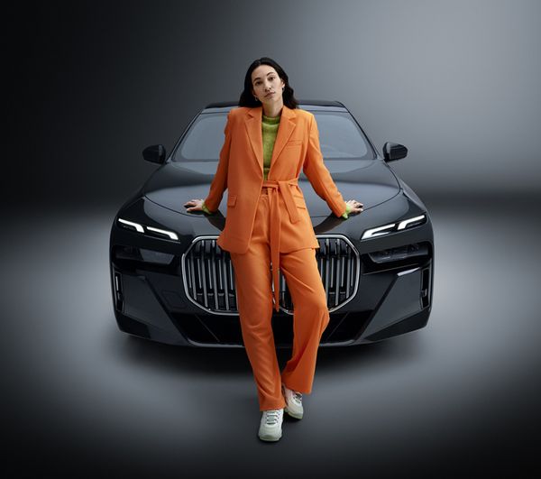 a woman in an orange suit standing in front of a company car