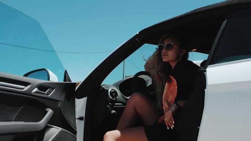 Women in a grey car sitting in driver's seat, with the door open